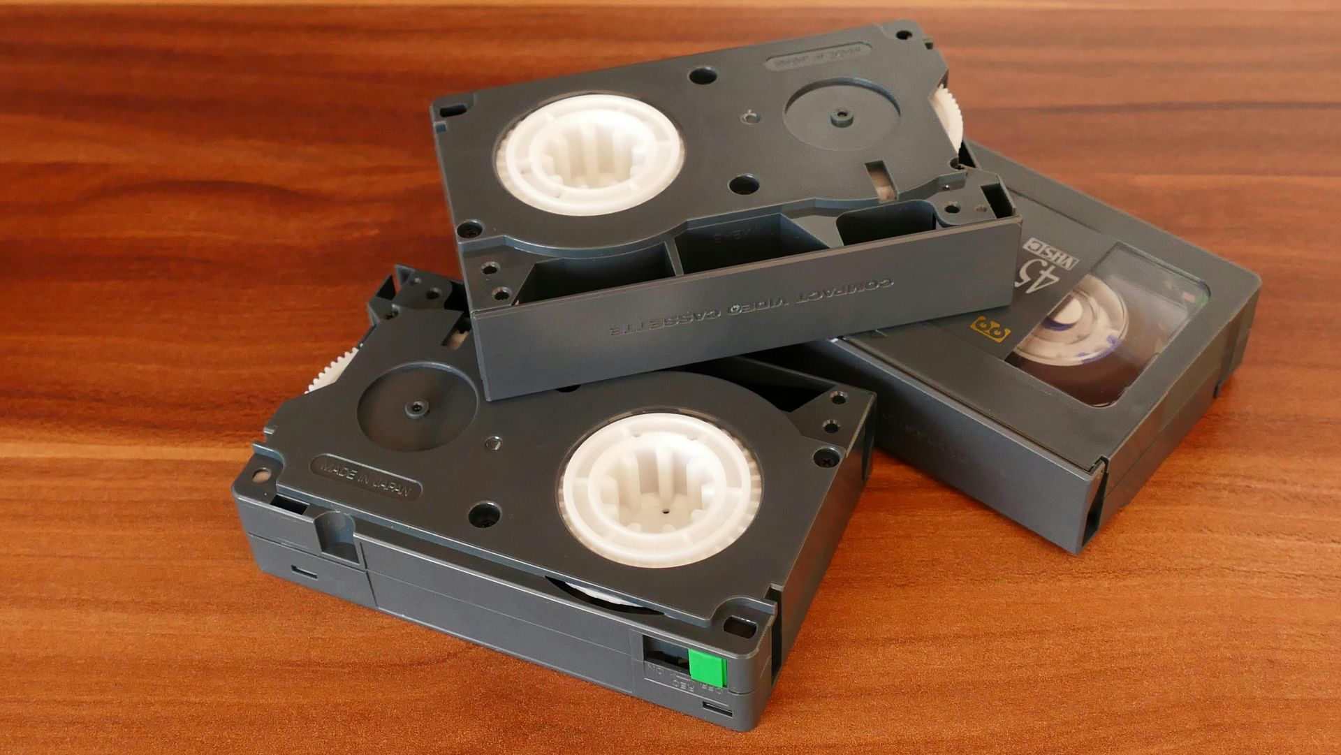Stacked VHS videotapes on a wooden surface, with one tape showing its white reels.