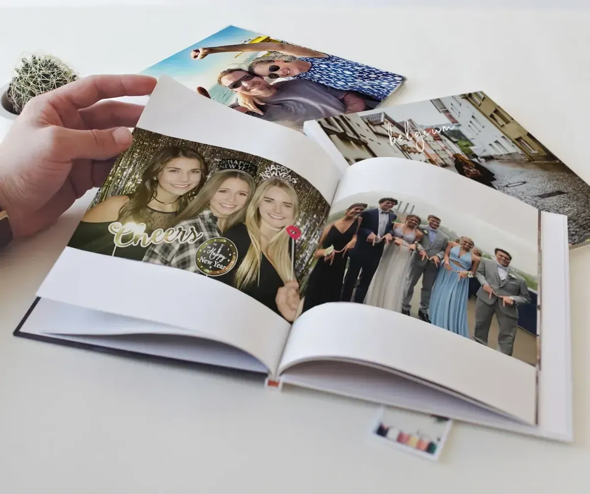 Hand turning pages of a photo book with colorful family and group photos on a white table