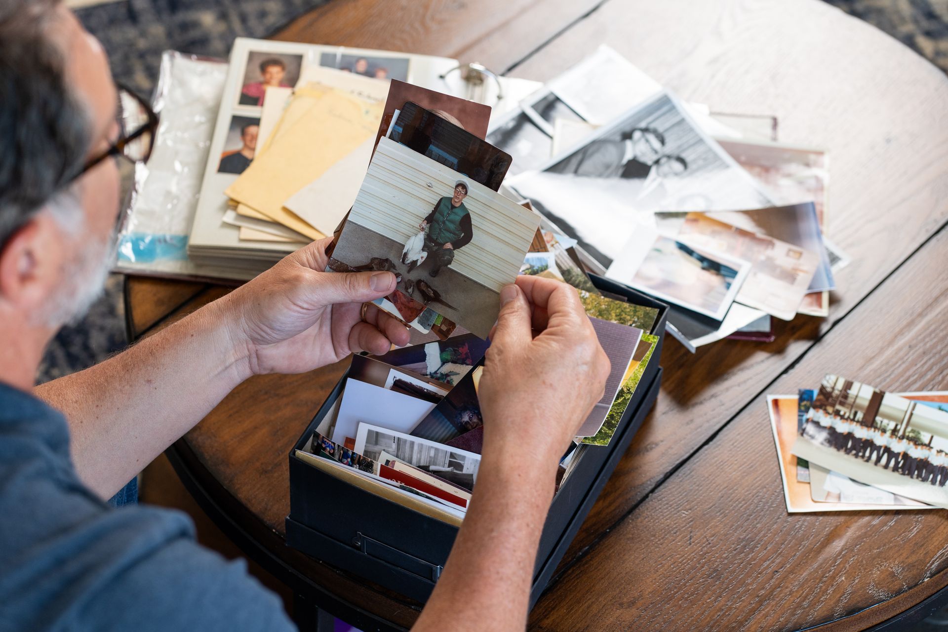 Person sorting printed photos on a wooden table beside an open photo album.