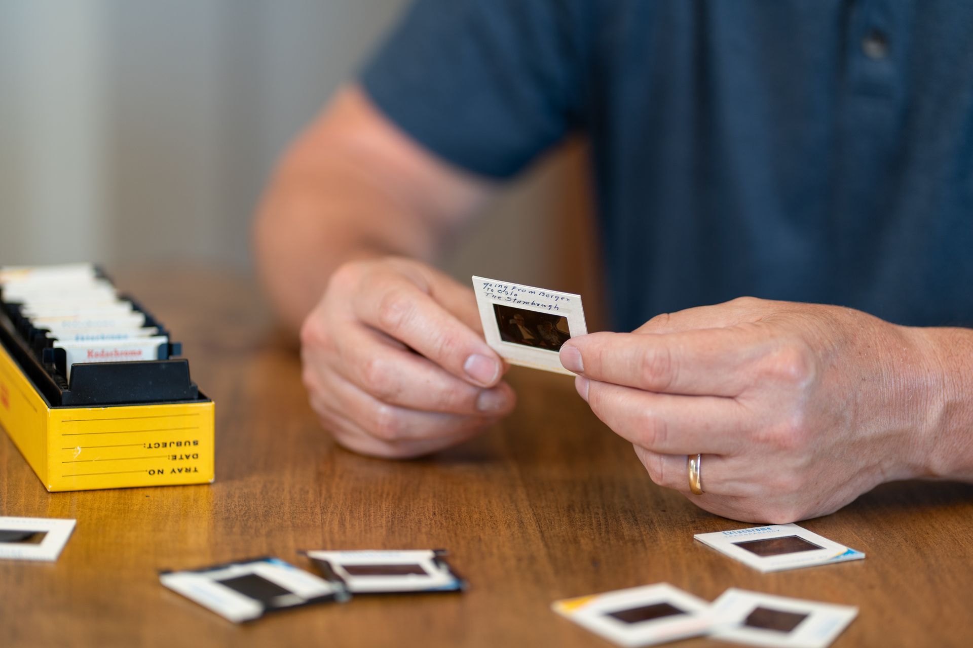 Hands holding a small slide on a wooden table with scattered slides and a yellow slide tray