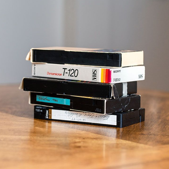 Stack of vintage VHS tapes on a wooden table, with a gray background.
