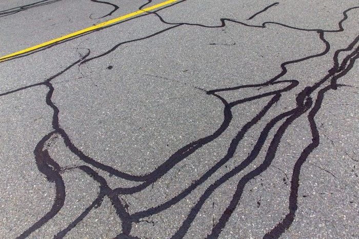 Asphalt road with dark sealant filling cracks. Yellow line in the top left.