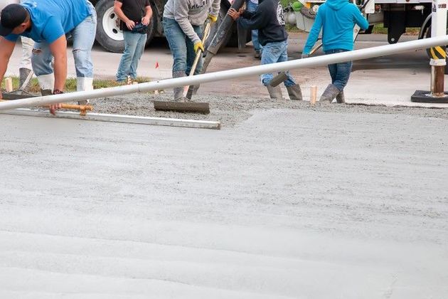 Construction workers pouring and leveling wet concrete on a road.