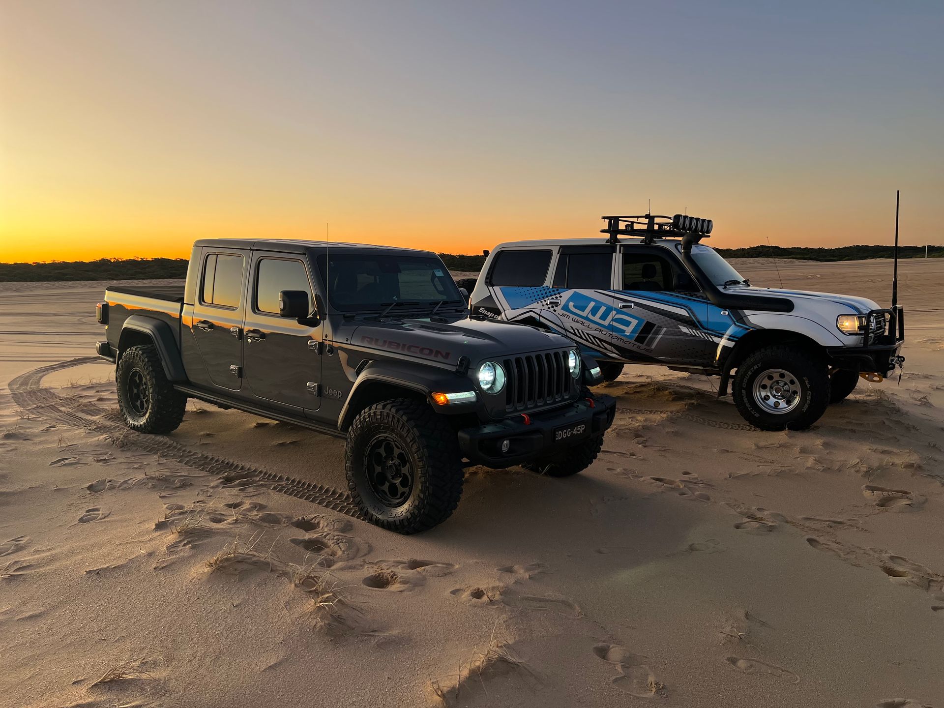 Two work vehicles parked on sand at sunset — Jim Wall Automotive in Mittagong, NSW