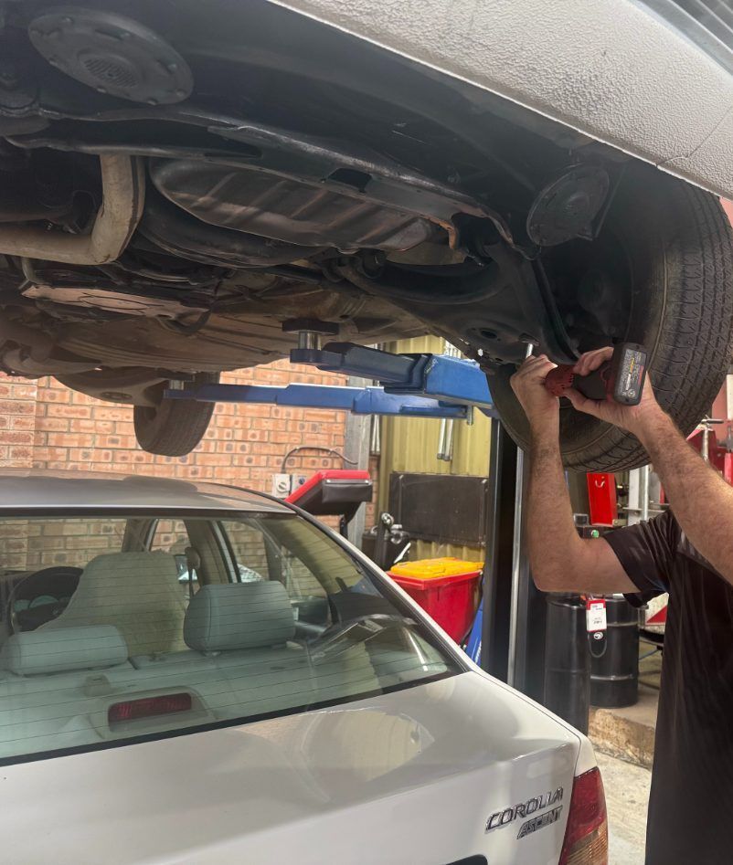 A Man is working under a hoisted car — Jim Wall Automotive in Moss Vale, NSW