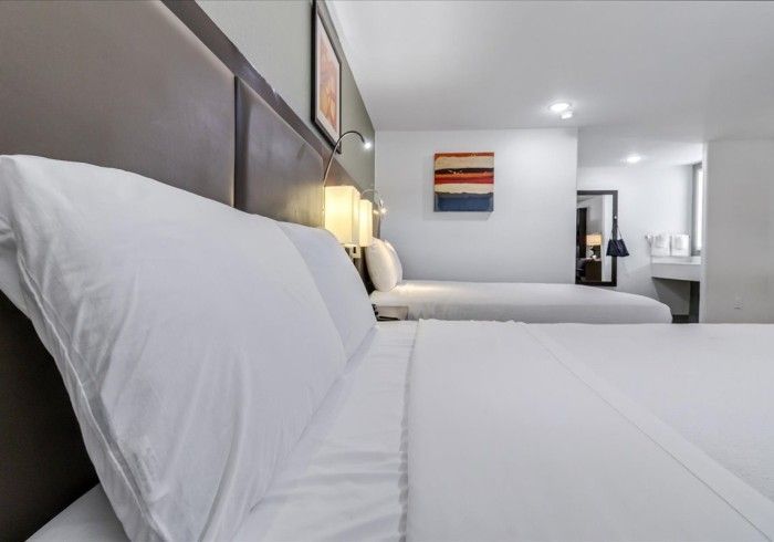 A hotel room interior featuring two neatly made beds with white linens, brown headboards, and abstract wall art.