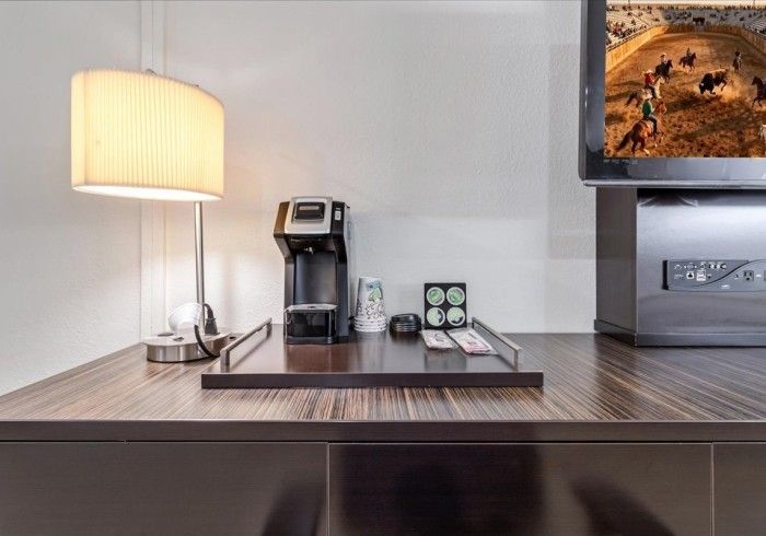 A hotel desk with a lamp, a coffee maker, and a TV showing a horse racing program on a dark wood surface.