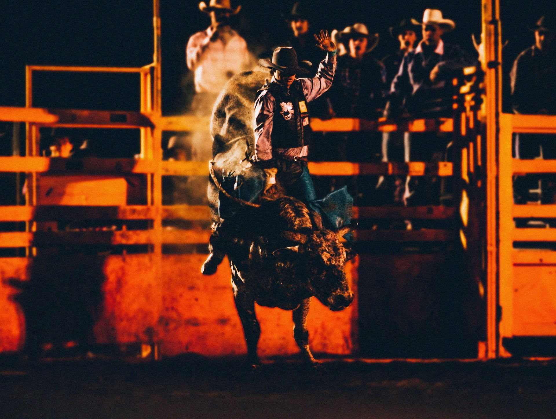 A cowboy riding a bucking bull at a rodeo under dramatic amber lighting