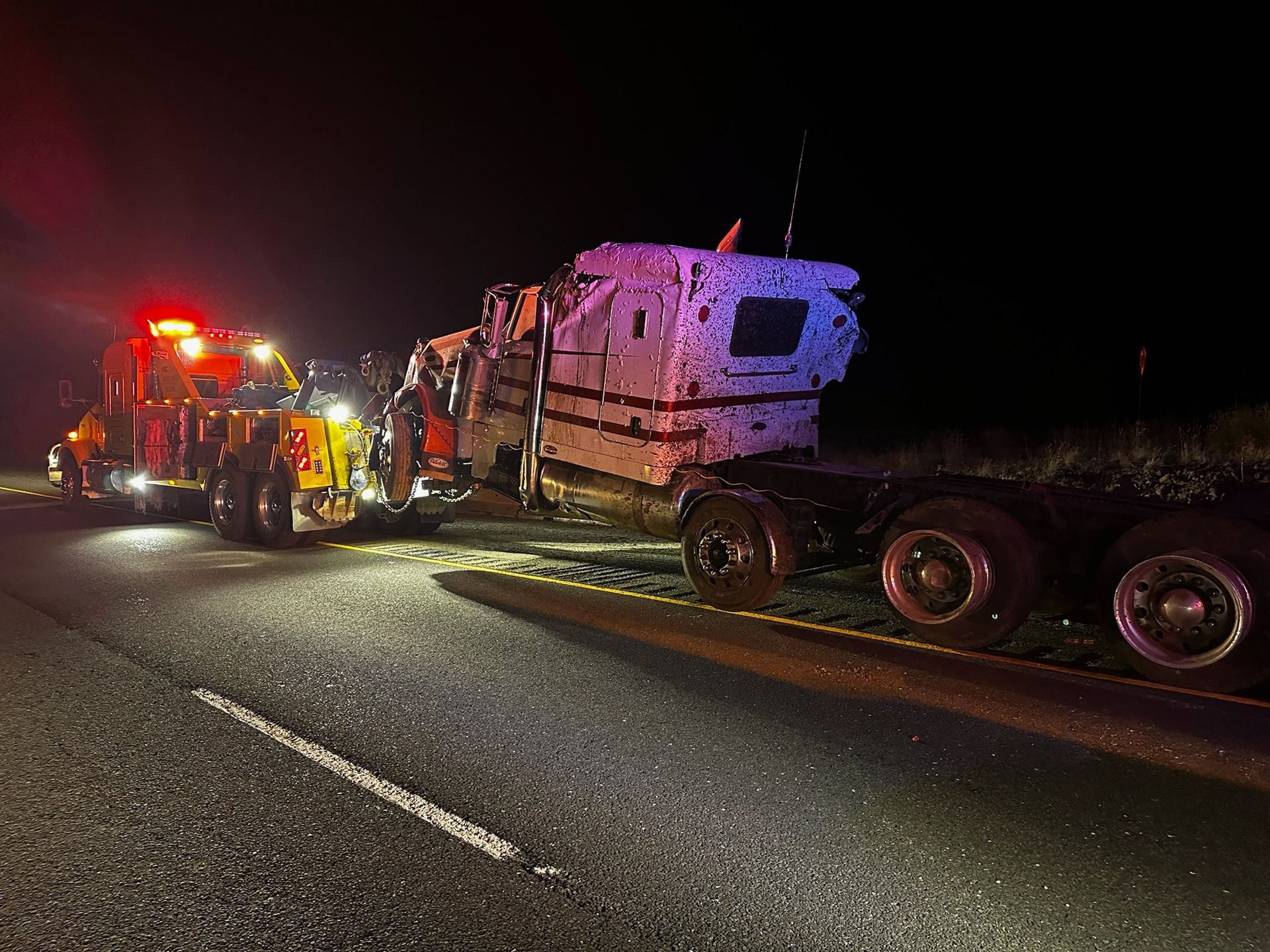 A tow truck is towing a camper down a highway at night.