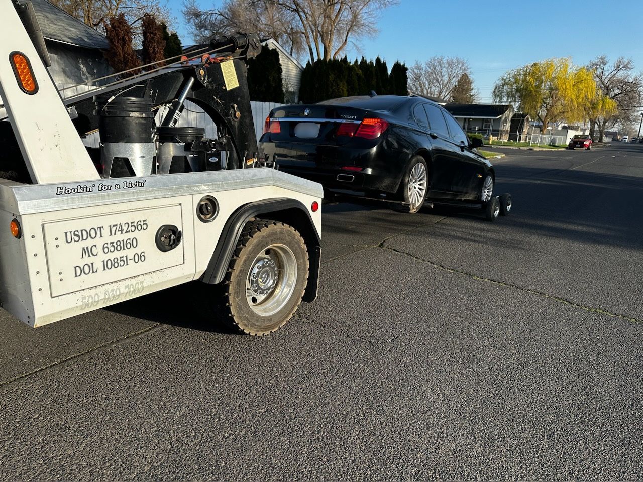 A tow truck is towing a black car down a street.