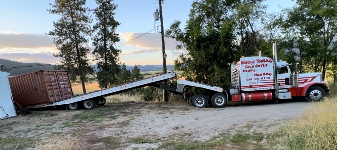 A tow truck is carrying a container on a trailer.