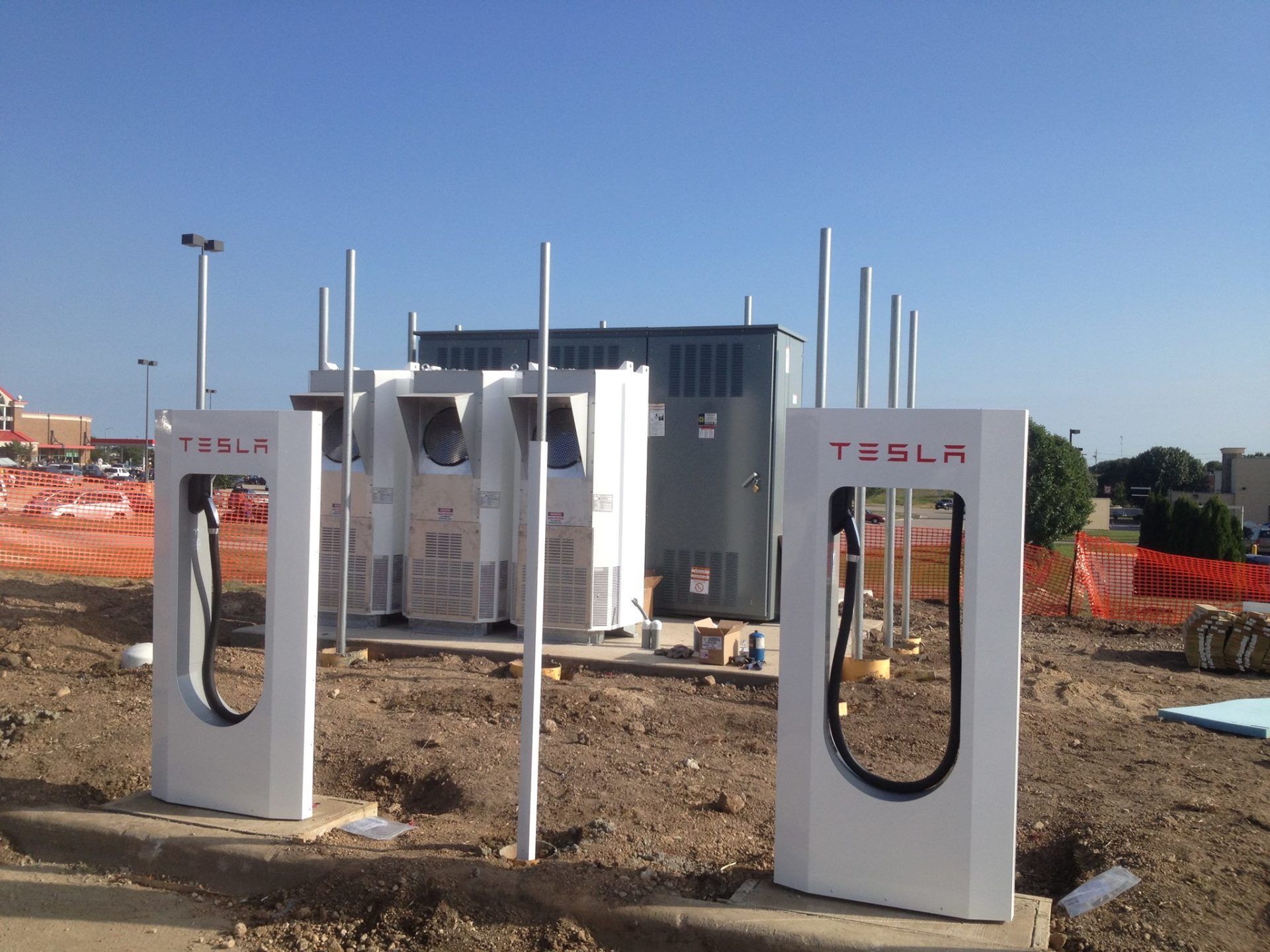 Tesla Supercharger site under construction with white charging stalls and orange safety fencing