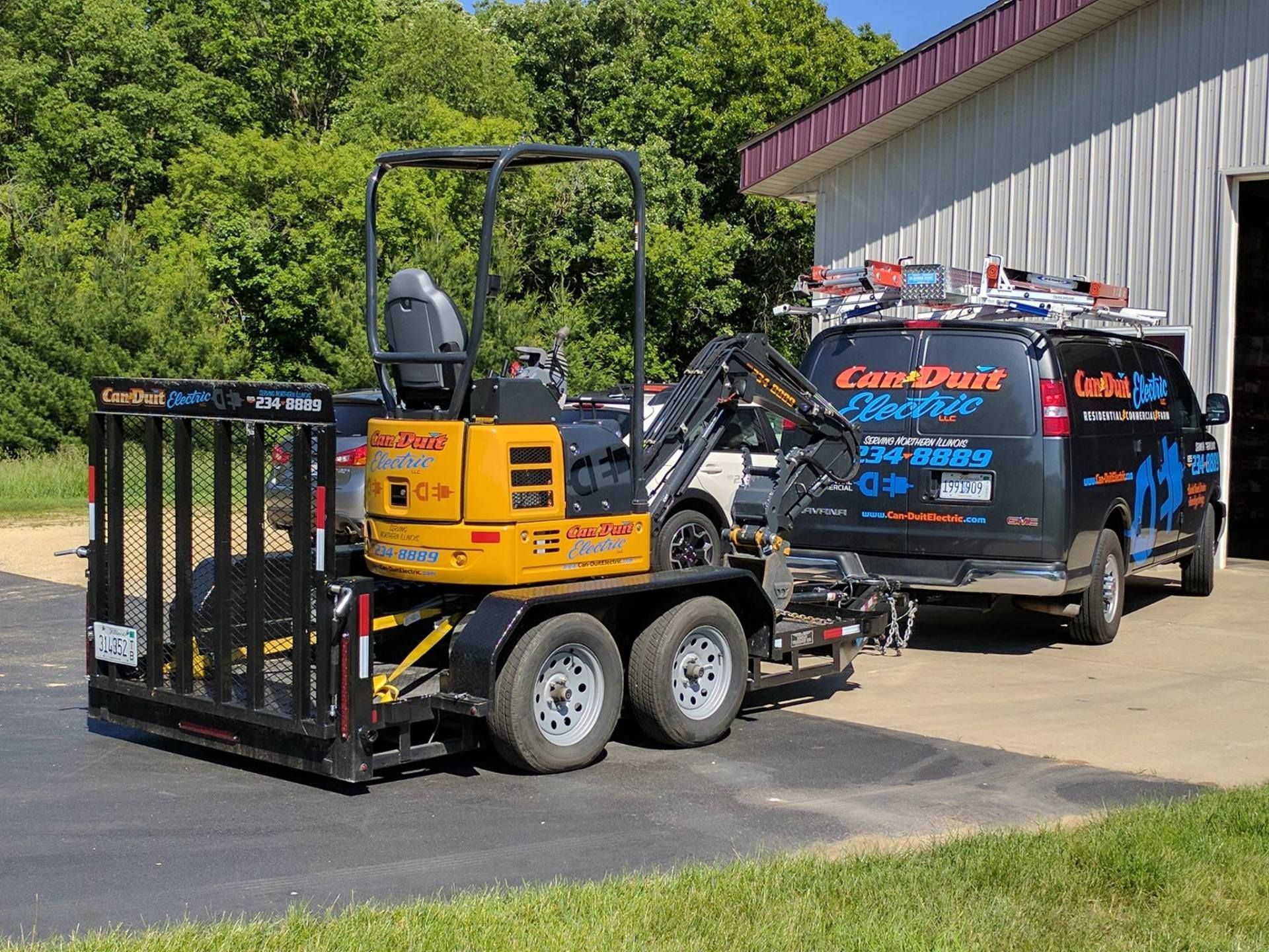 Yellow mini excavator with grapple trailer hitched to a blue work van in a driveway