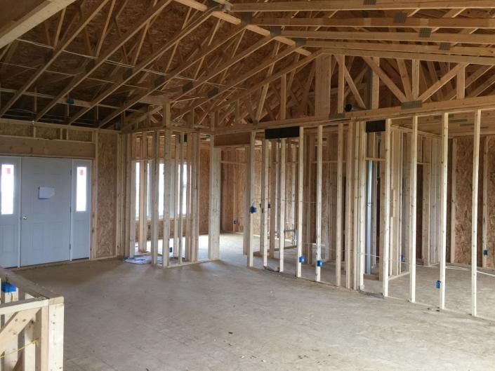 Unfinished house interior with exposed wooden framing, trusses, and a concrete floor