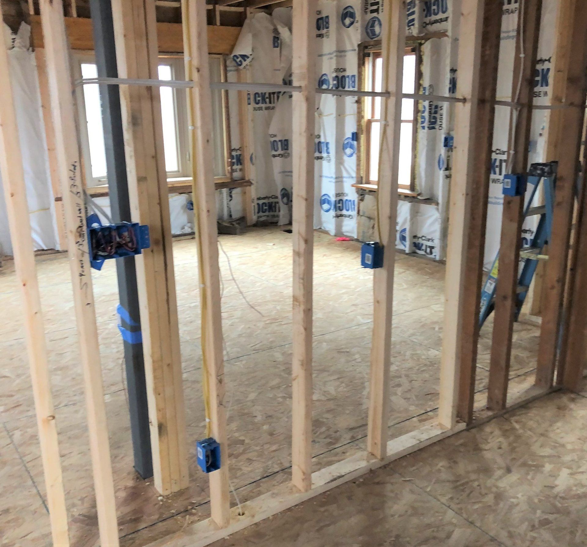 Framed interior under construction with exposed studs, insulation, and rough subflooring.