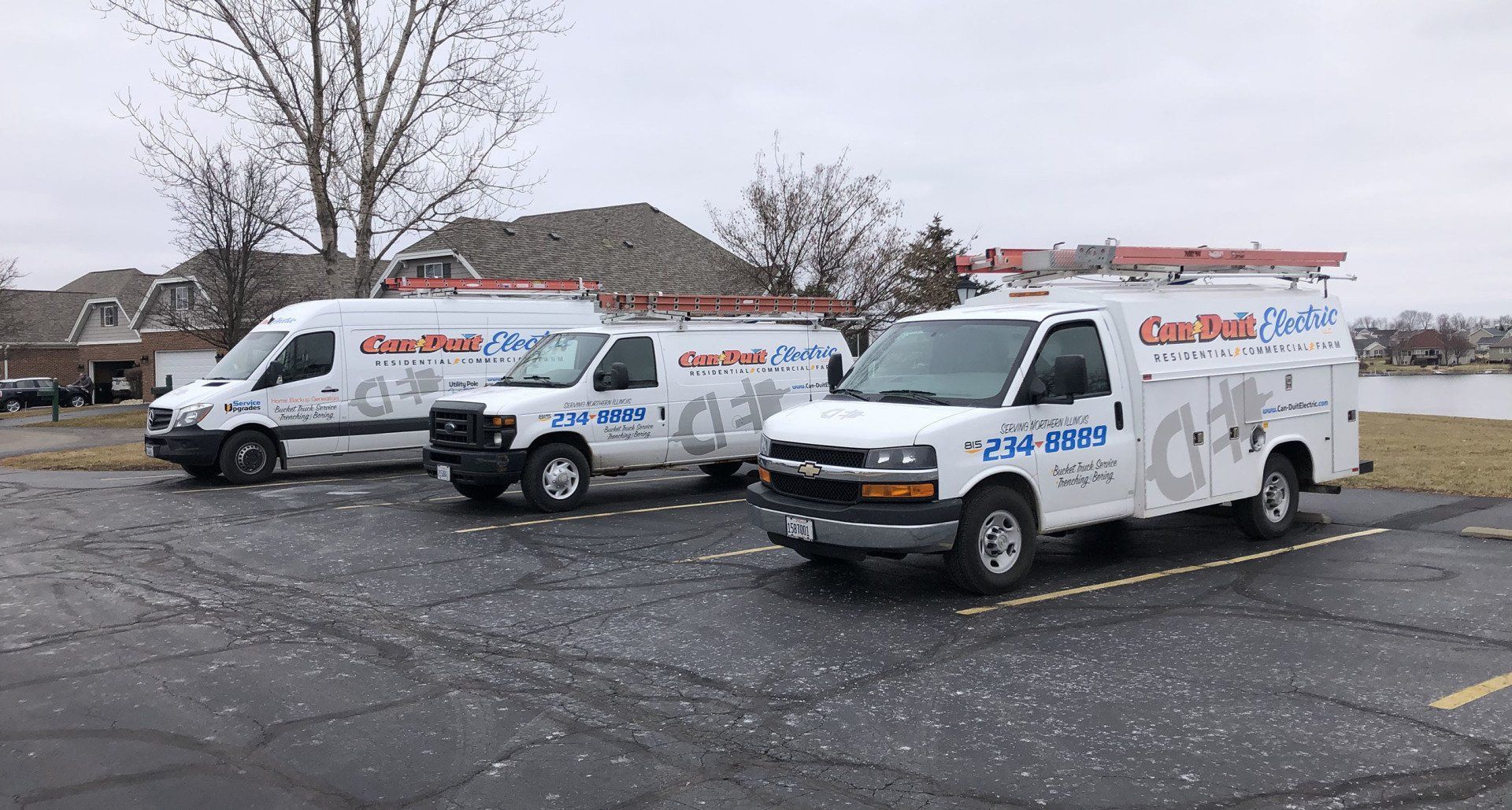 Three white utility vans parked in a snowy lot on a cloudy day