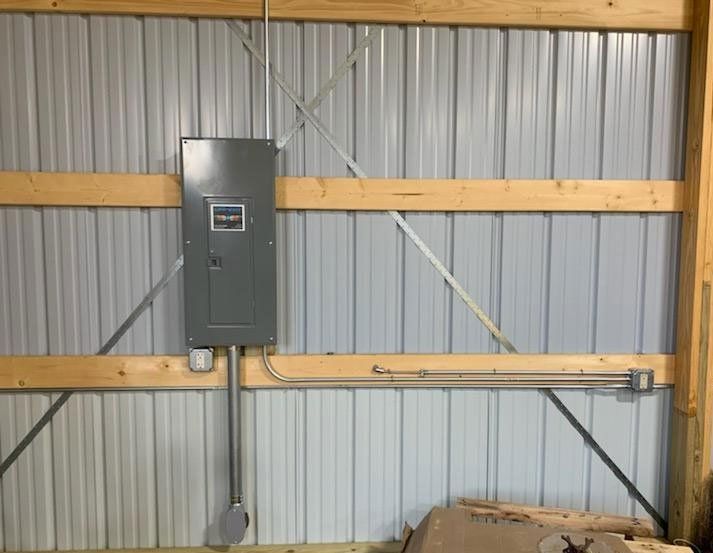 Gray electrical panel on corrugated metal wall with conduit and wooden braces in a utility space