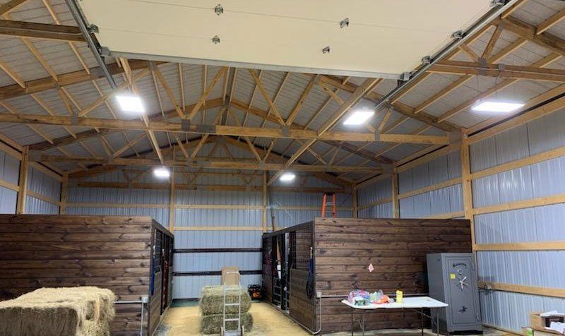Rustic barn interior with wood stalls, hay bales, and high metal roof lighting.