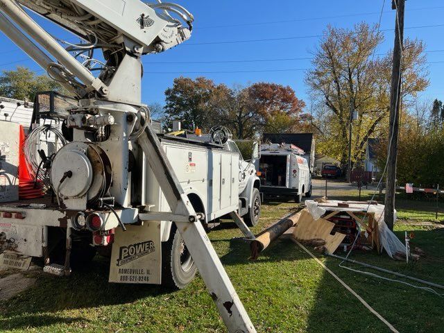Utility truck with boom arm parked on grass beside a house, with equipment and a tarp in the yard