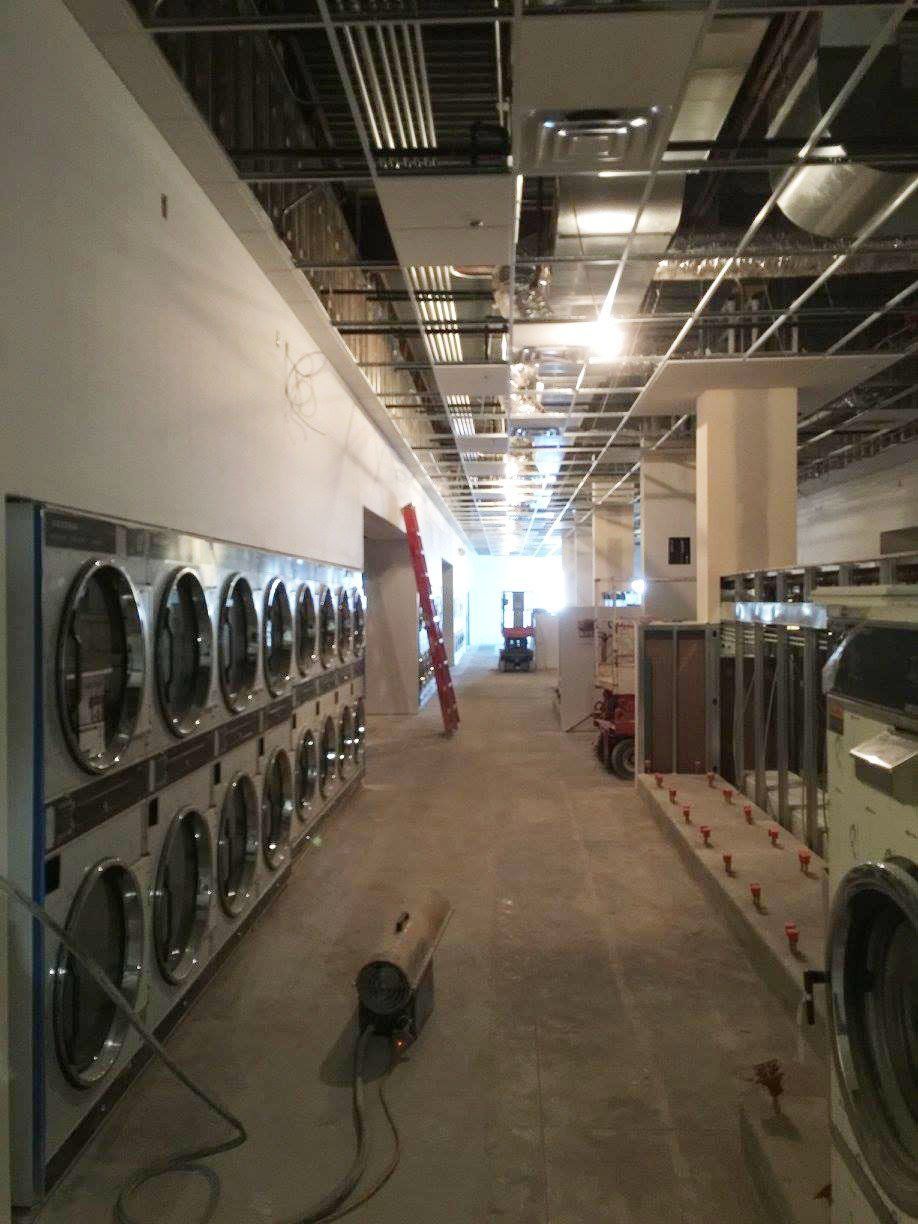 Laundry room under construction with rows of washers and exposed ceiling ducts