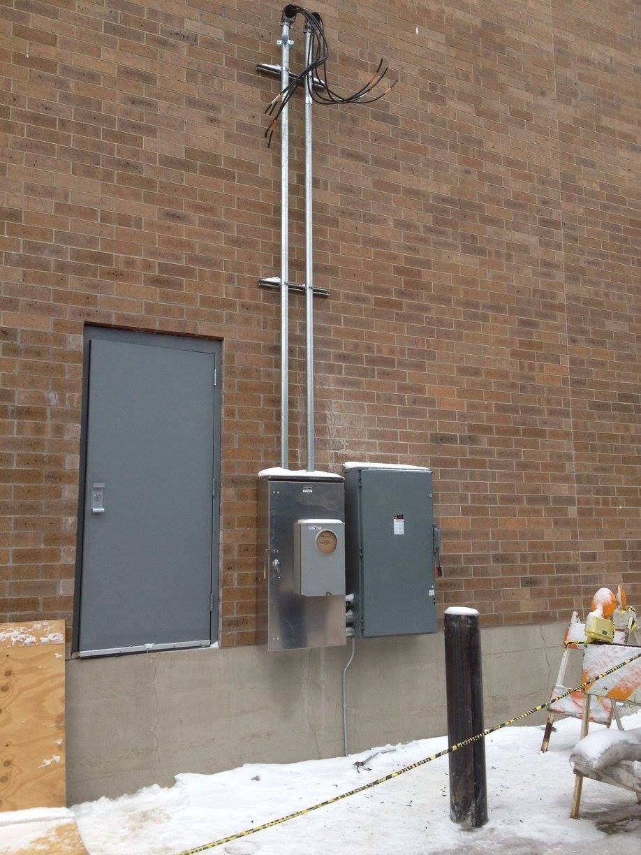 Utility boxes and conduit mounted on a brick building beside a gray door.