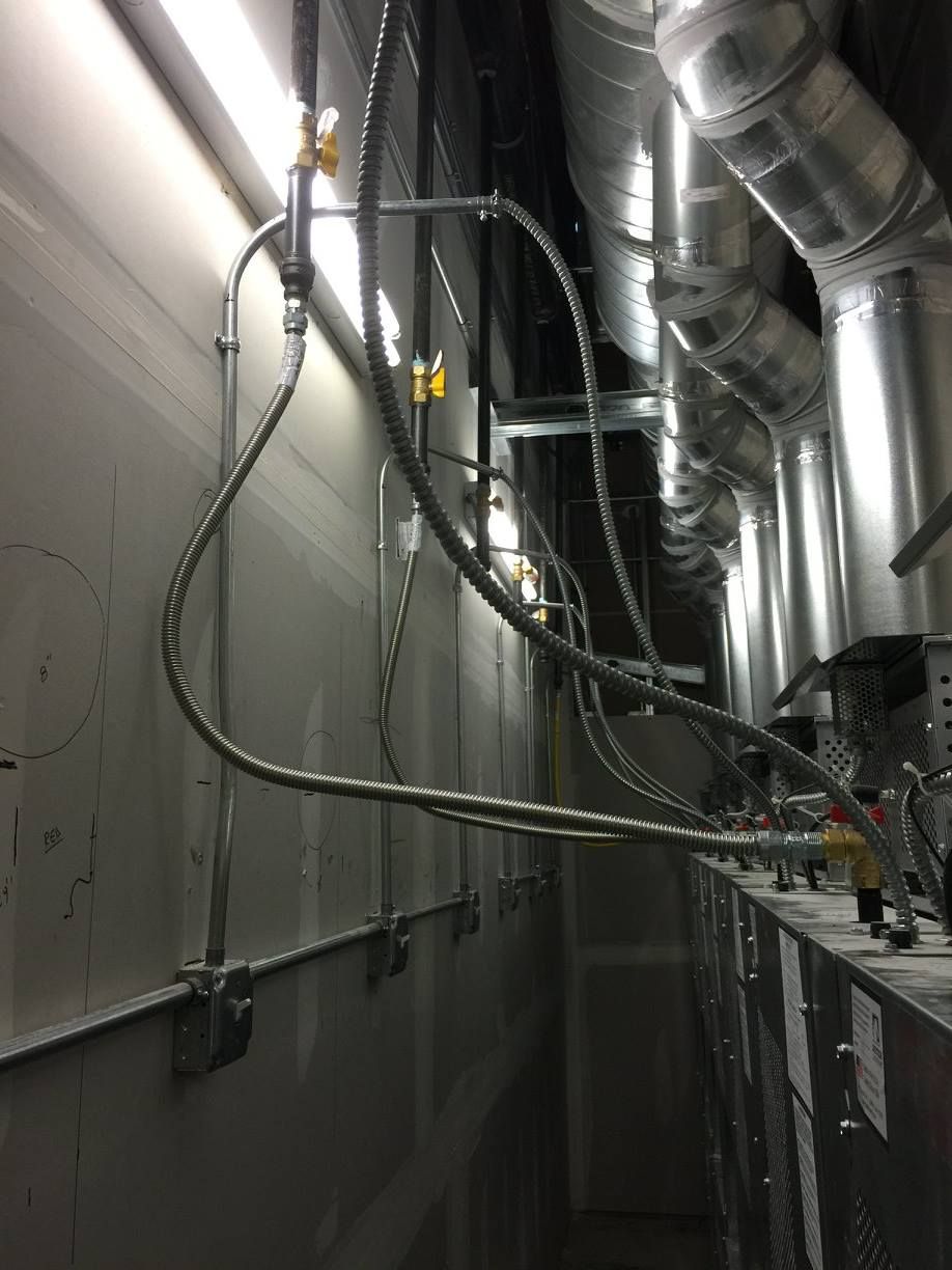 Narrow industrial utility corridor with silver ducts, black cables, and wall-mounted pipes overhead