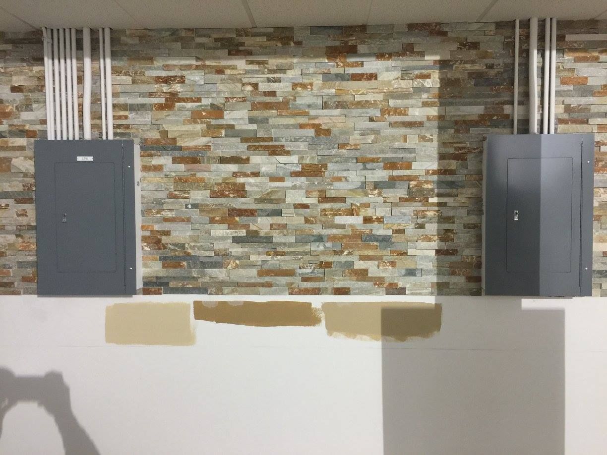 Wall-mounted gray cabinets on a stone-tiled wall above a white counter with paint samples.