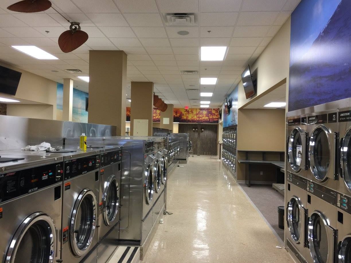 Laundry room with rows of stainless steel washers and dryers in a bright tiled space