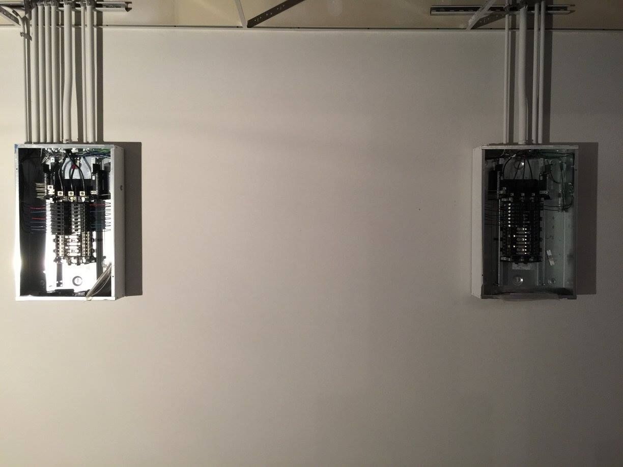 Two electrical breaker panels mounted on a wall, with conduit pipes running above them.