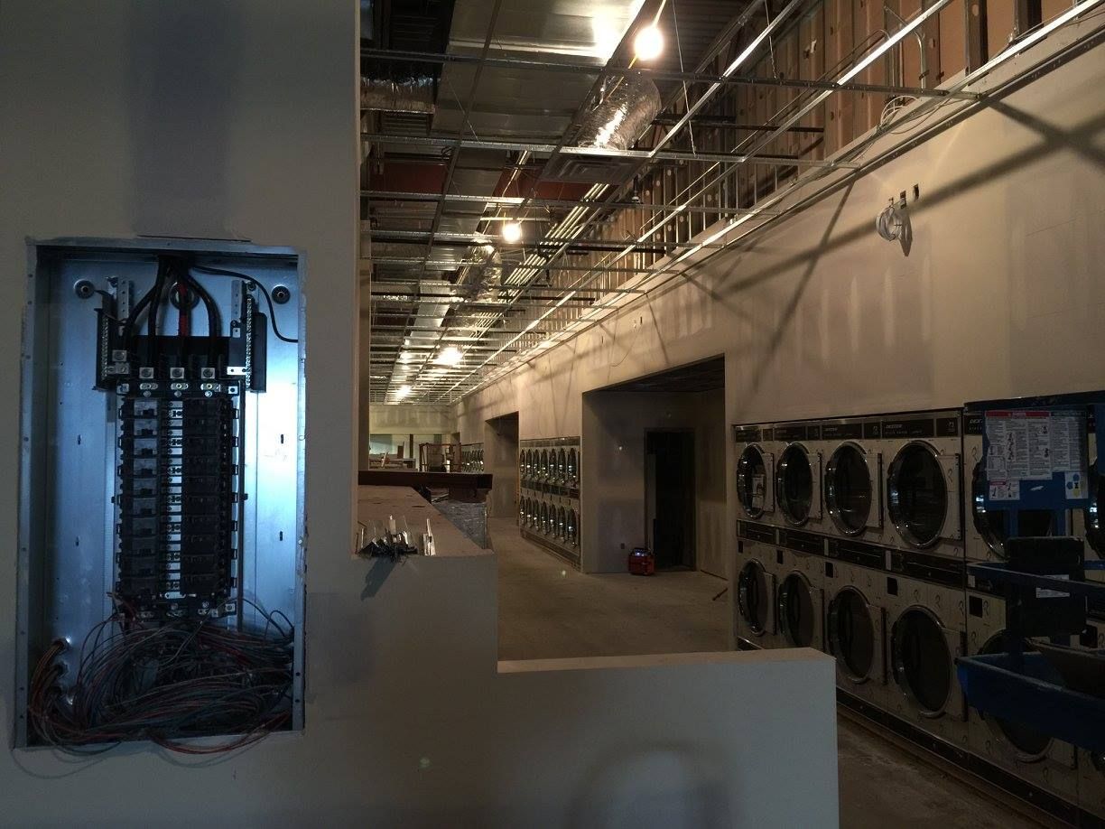 Industrial hallway with open electrical panel and rows of stacked HVAC/ventilation units along the wall