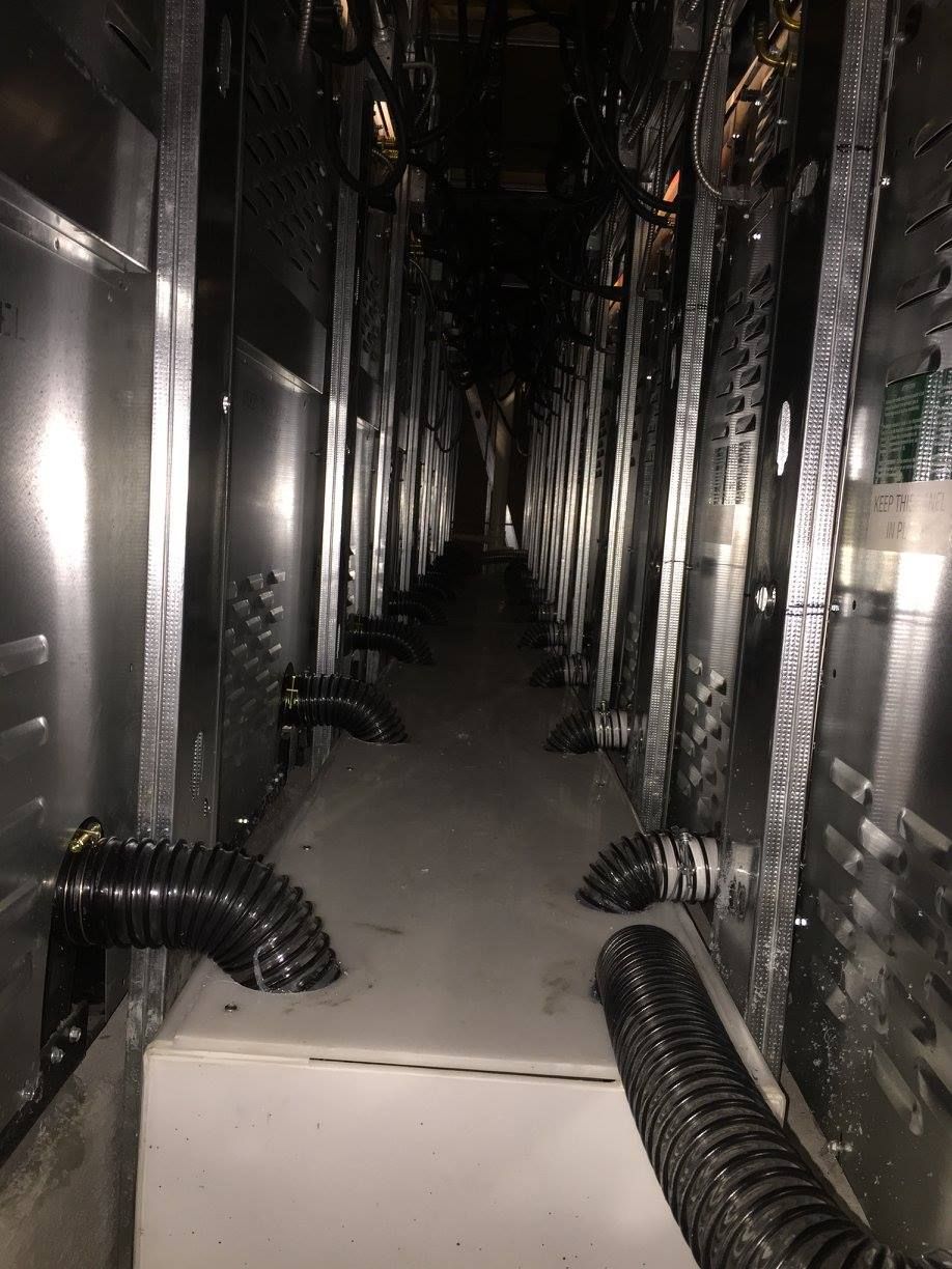 Narrow metal utility corridor with pipes and cables lining both sides, viewed from the center.