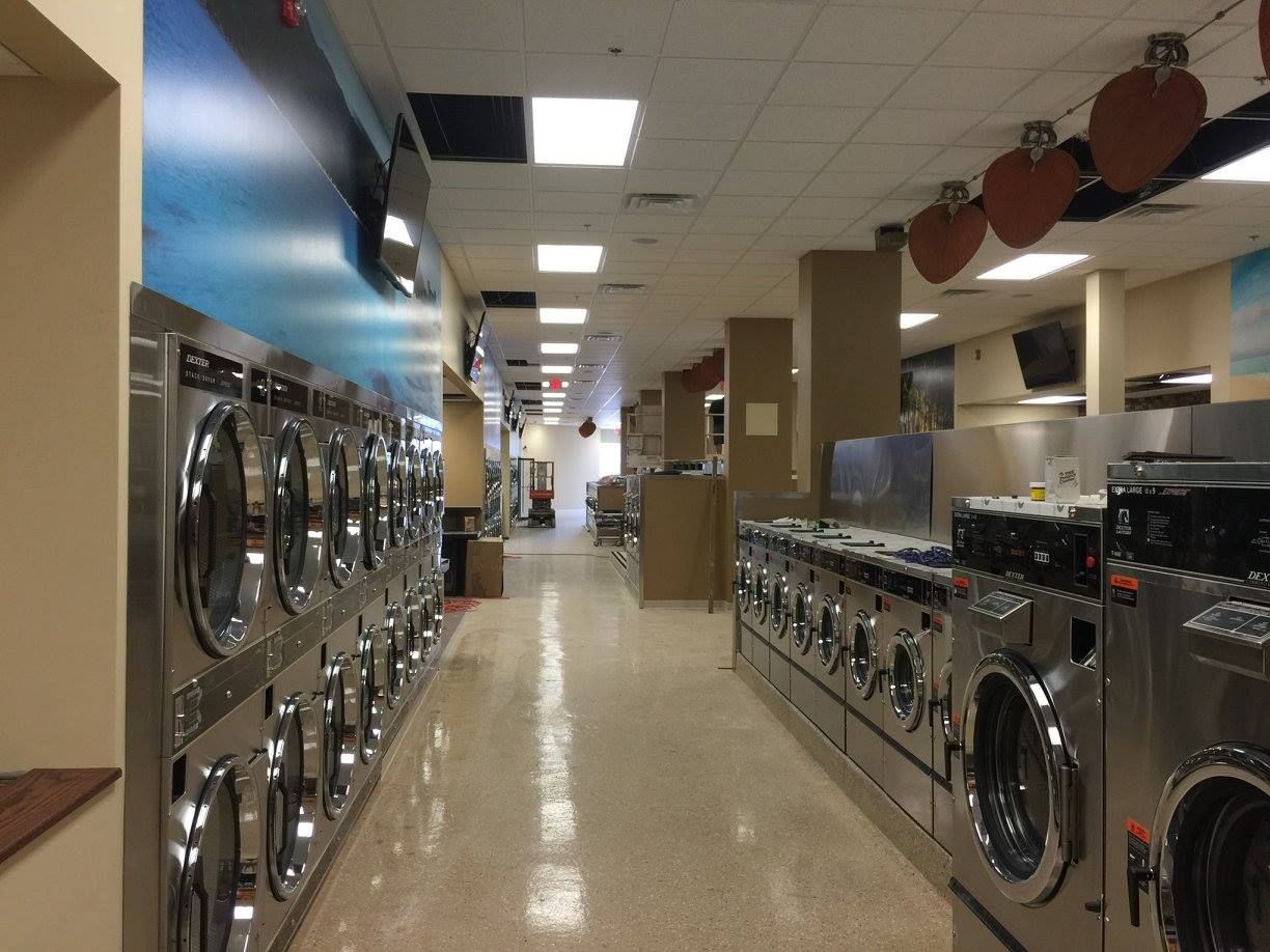 Laundry room aisle with rows of front-loading washers and dryers under fluorescent lights