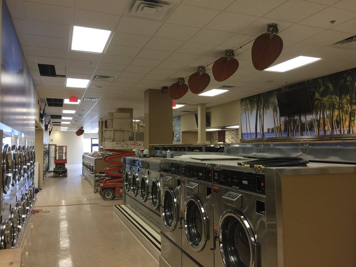 A laundromat aisle with rows of washing machines, bright ceiling lights, and baskets in the back.