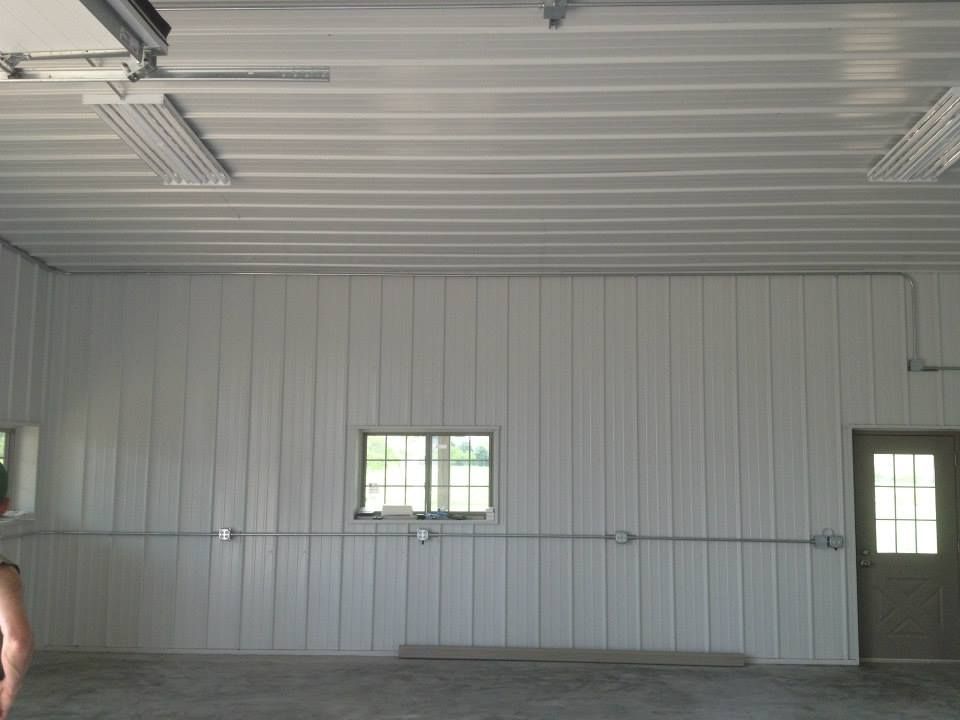 Empty metal garage with white walls, a small window, and a door on the right.