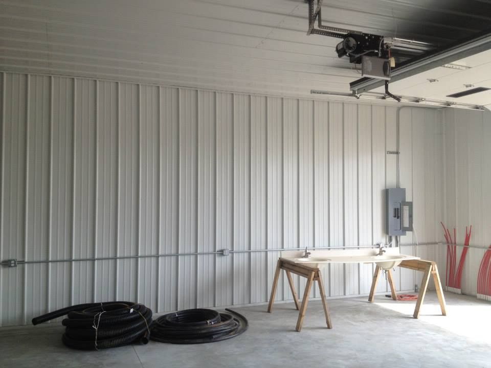 Garage interior with white corrugated wall, workbench, coiled hoses, and an open garage door opener overhead
