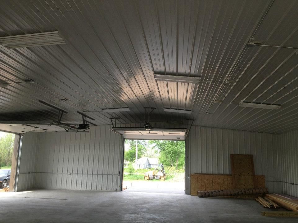 Empty metal building interior with open garage doors, workbench, and daylight outside