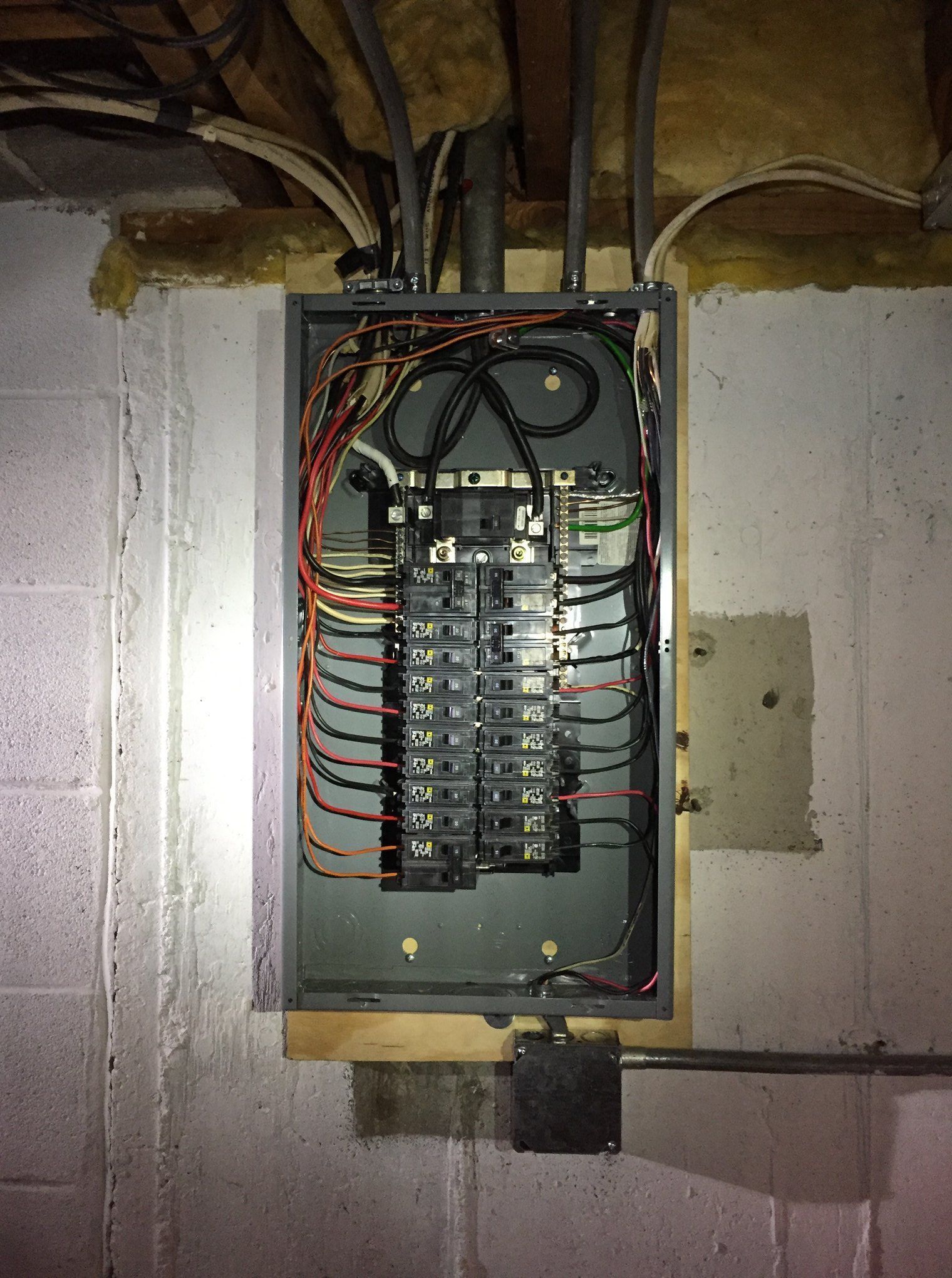 Open electrical breaker panel with exposed wiring in a basement wall.