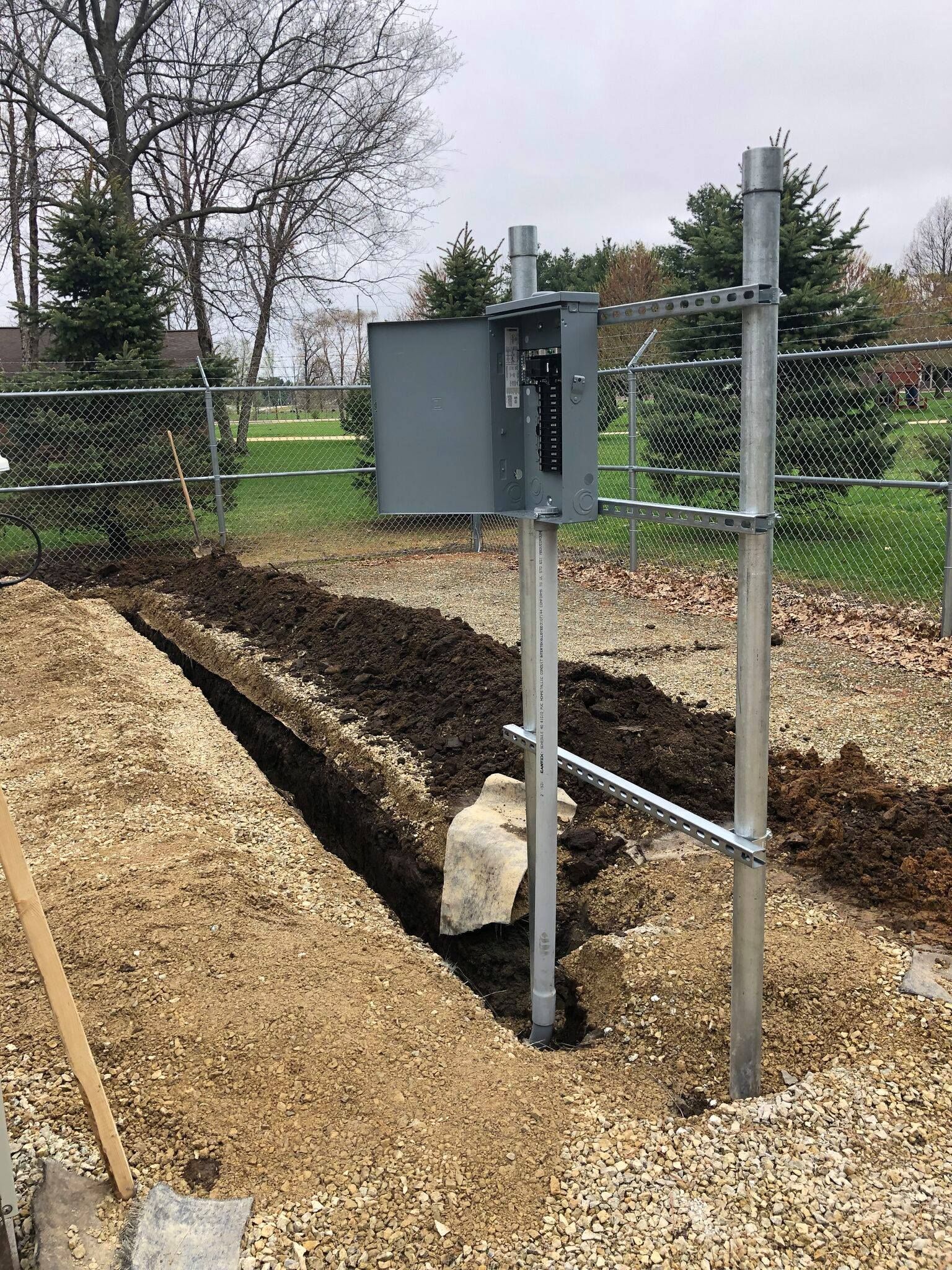 Utility box beside a fenced trench in a gravel-lined outdoor work area
