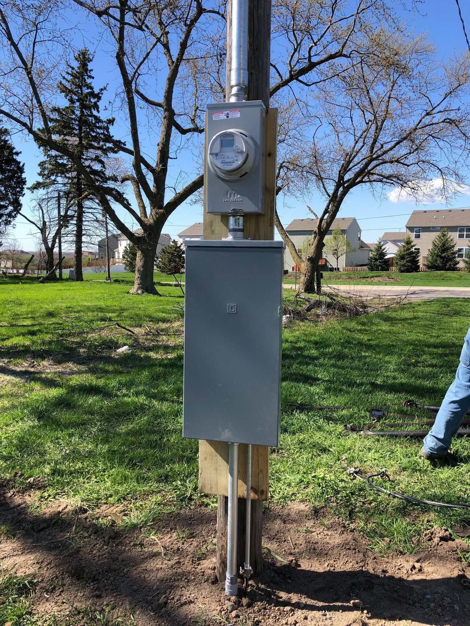 Outdoor electrical meter and gray utility box on a wooden post in a grassy park