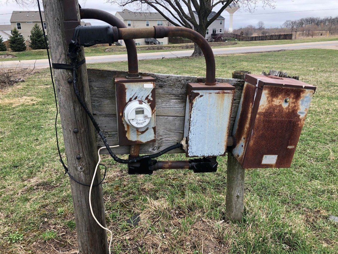Rusty roadside utility meter boxes mounted on a wooden post in a grassy field.