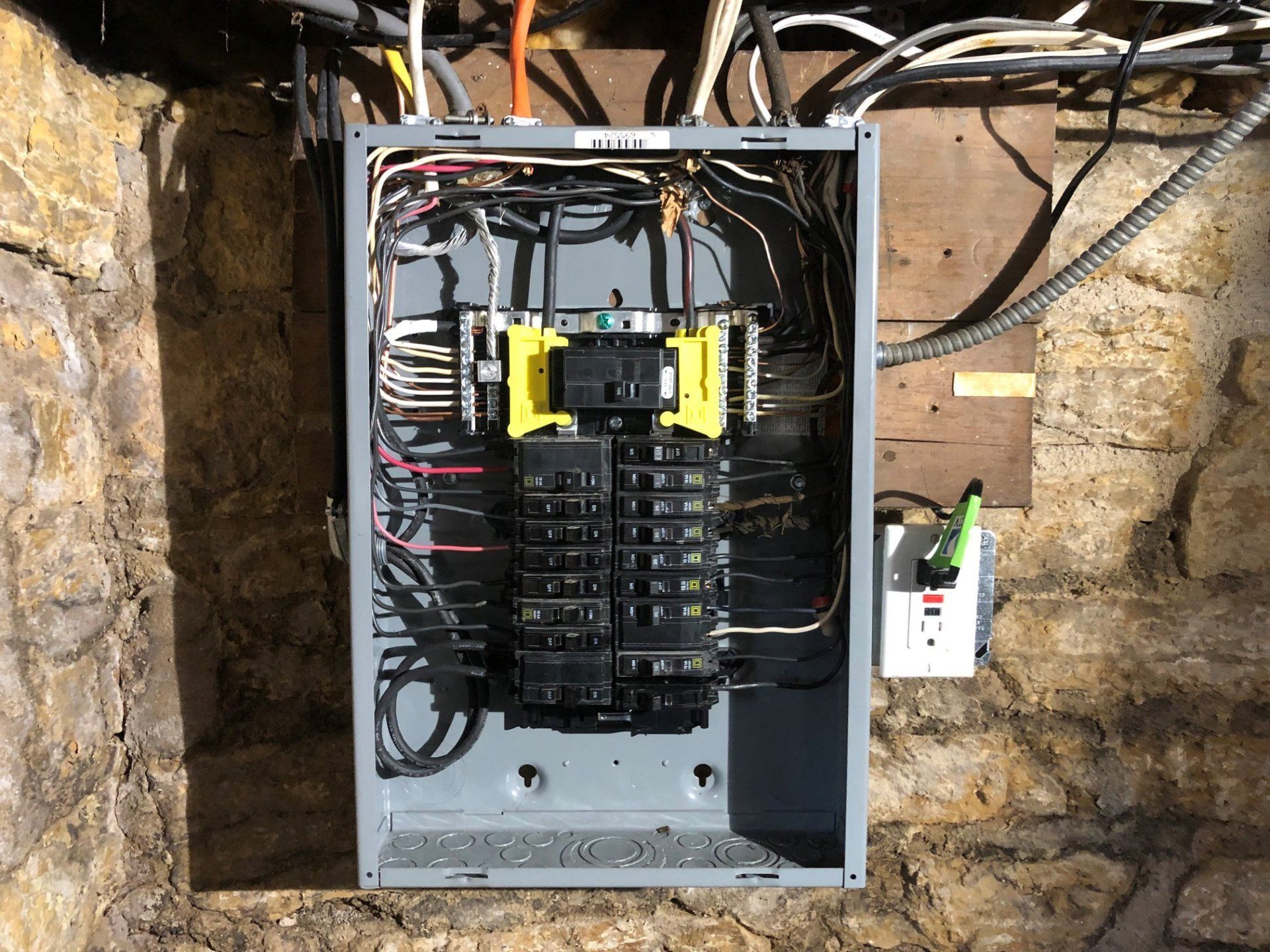 Open electrical breaker panel in a wall cavity with exposed wiring and insulation.