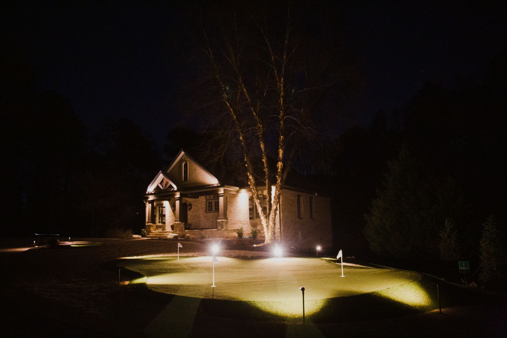 House with warm exterior lights and illuminated putt putt course at night