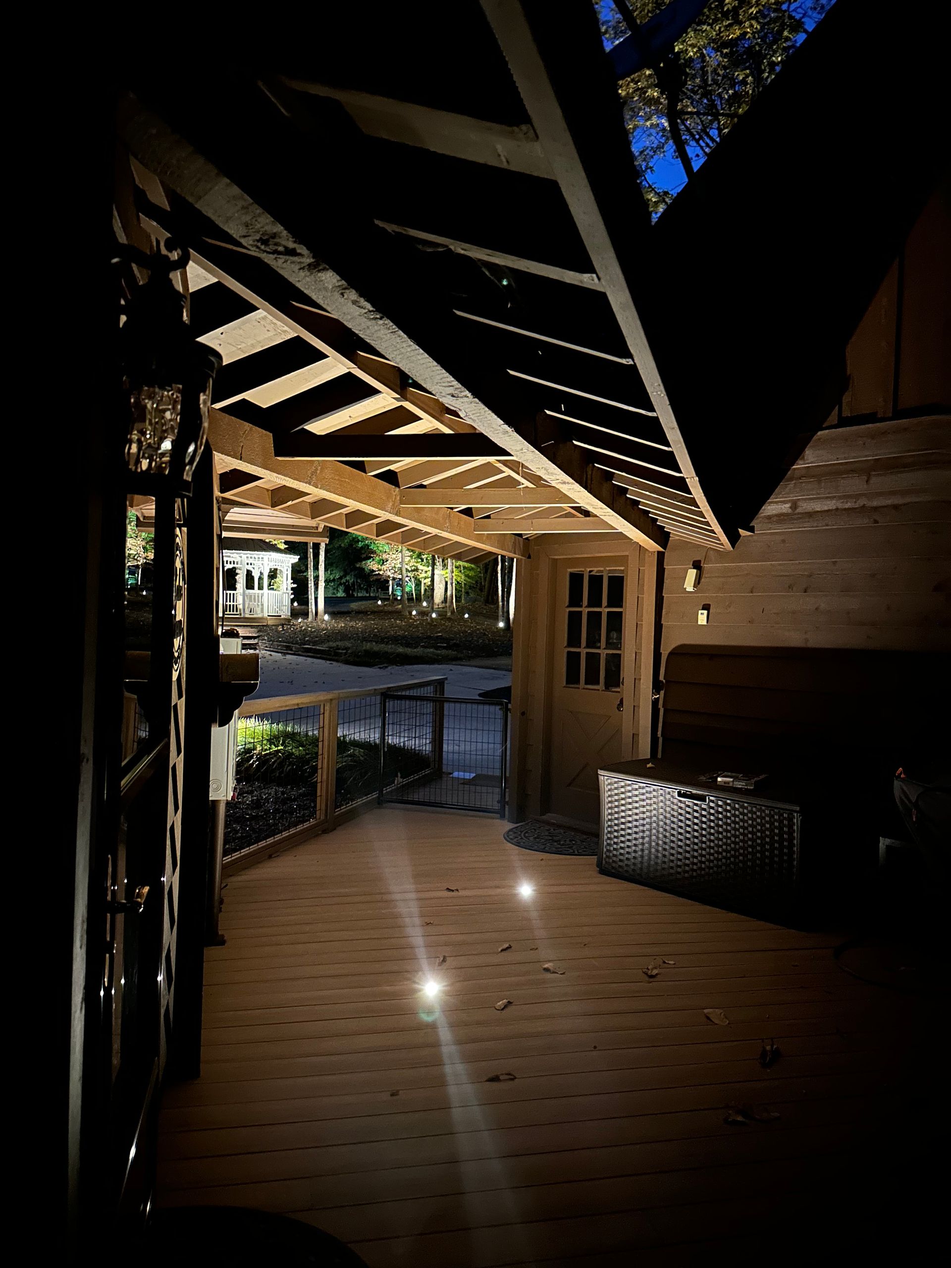 Wooden porch with lights, leading to a door; dark interior with distant greenery visible.