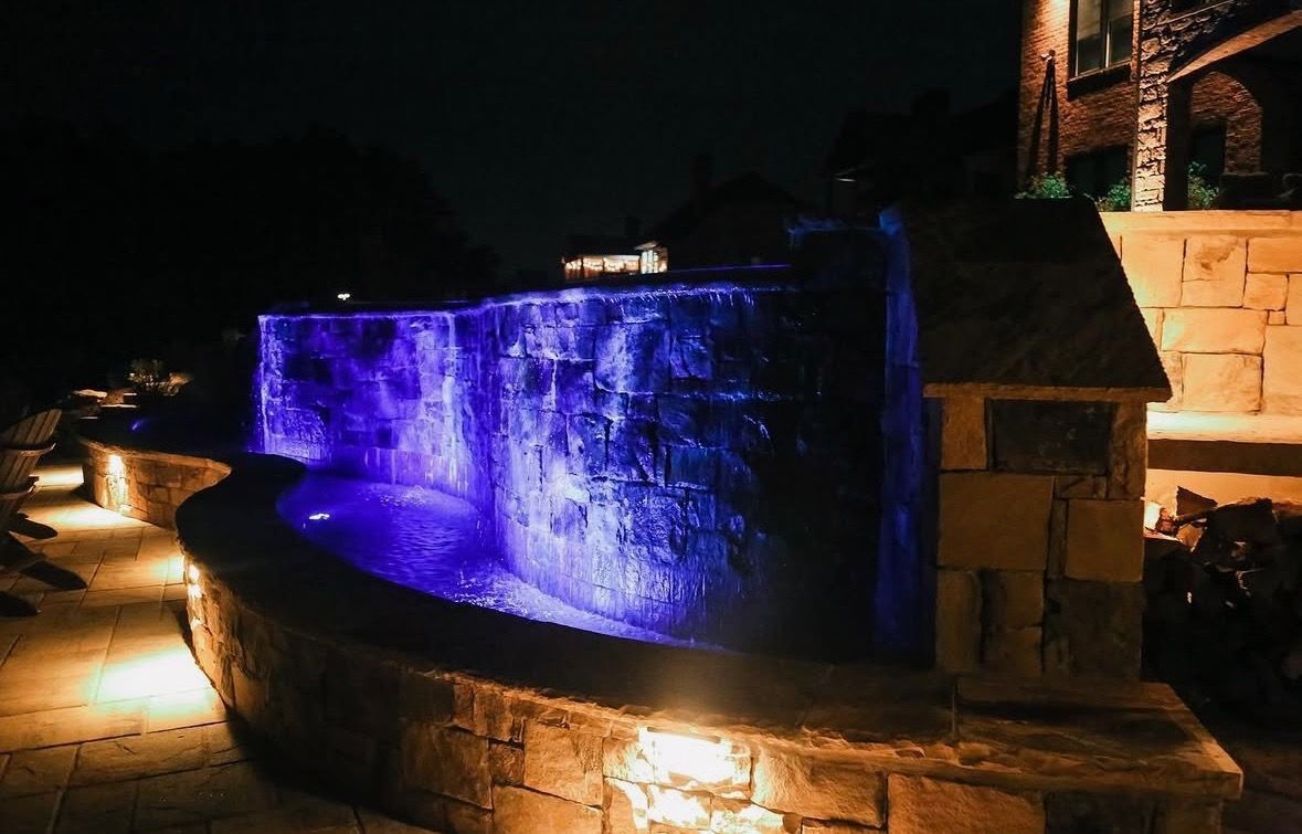 Illuminated blue-lit waterfall wall at night beside a stone walkway