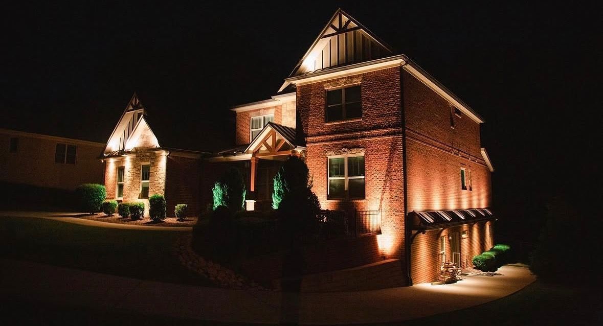 Night-lit brick house with warm exterior lighting and a small front yard