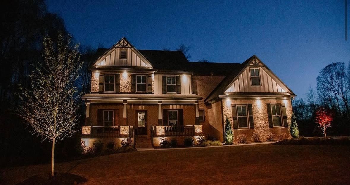 Large illuminated house at night with warm lights and bare trees in the yard