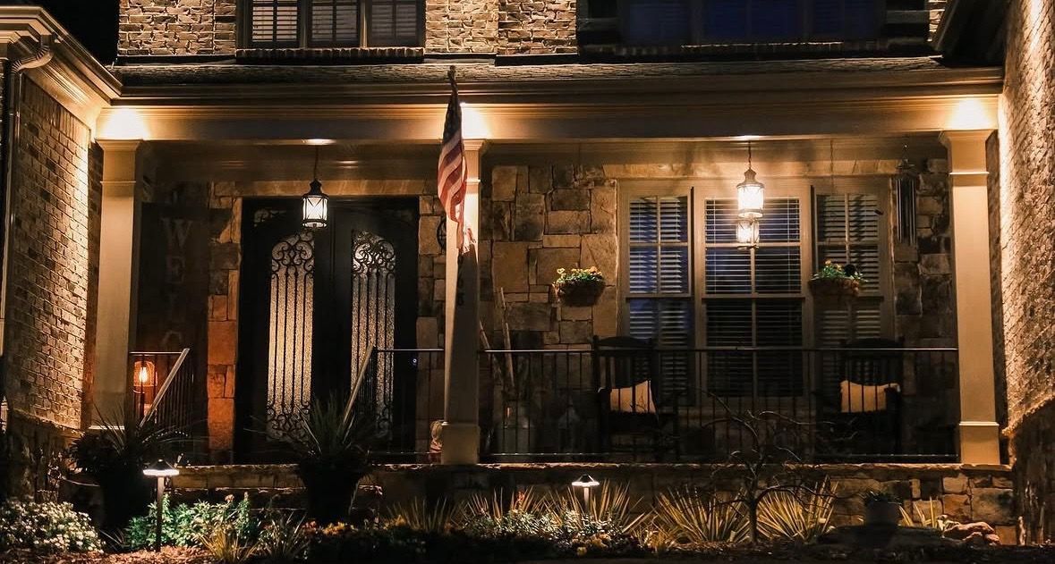 Warmly lit townhouse façade with ornate double doors, shutters, and a small front porch at night