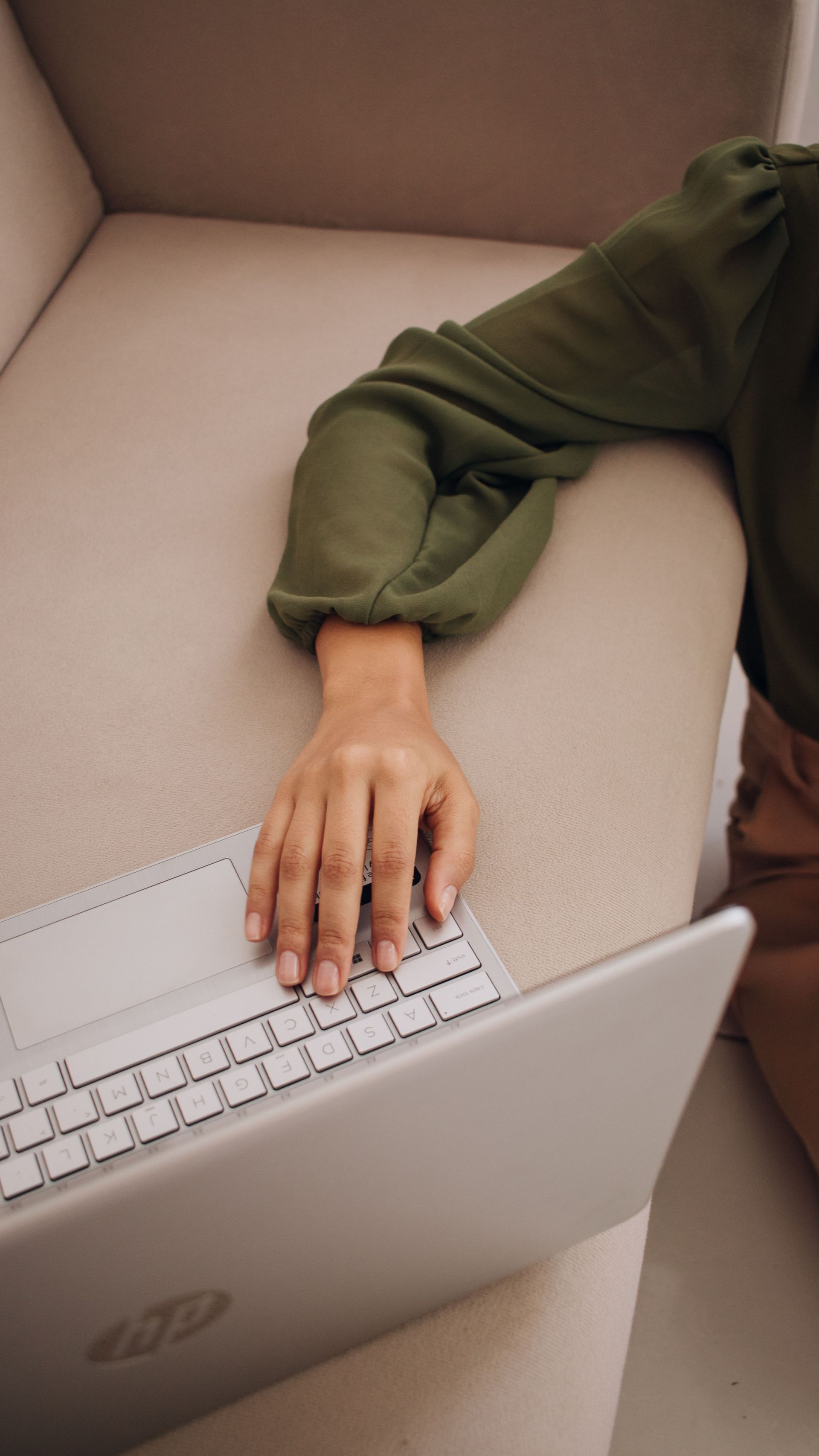 Person in green sweater using a laptop on a beige couch