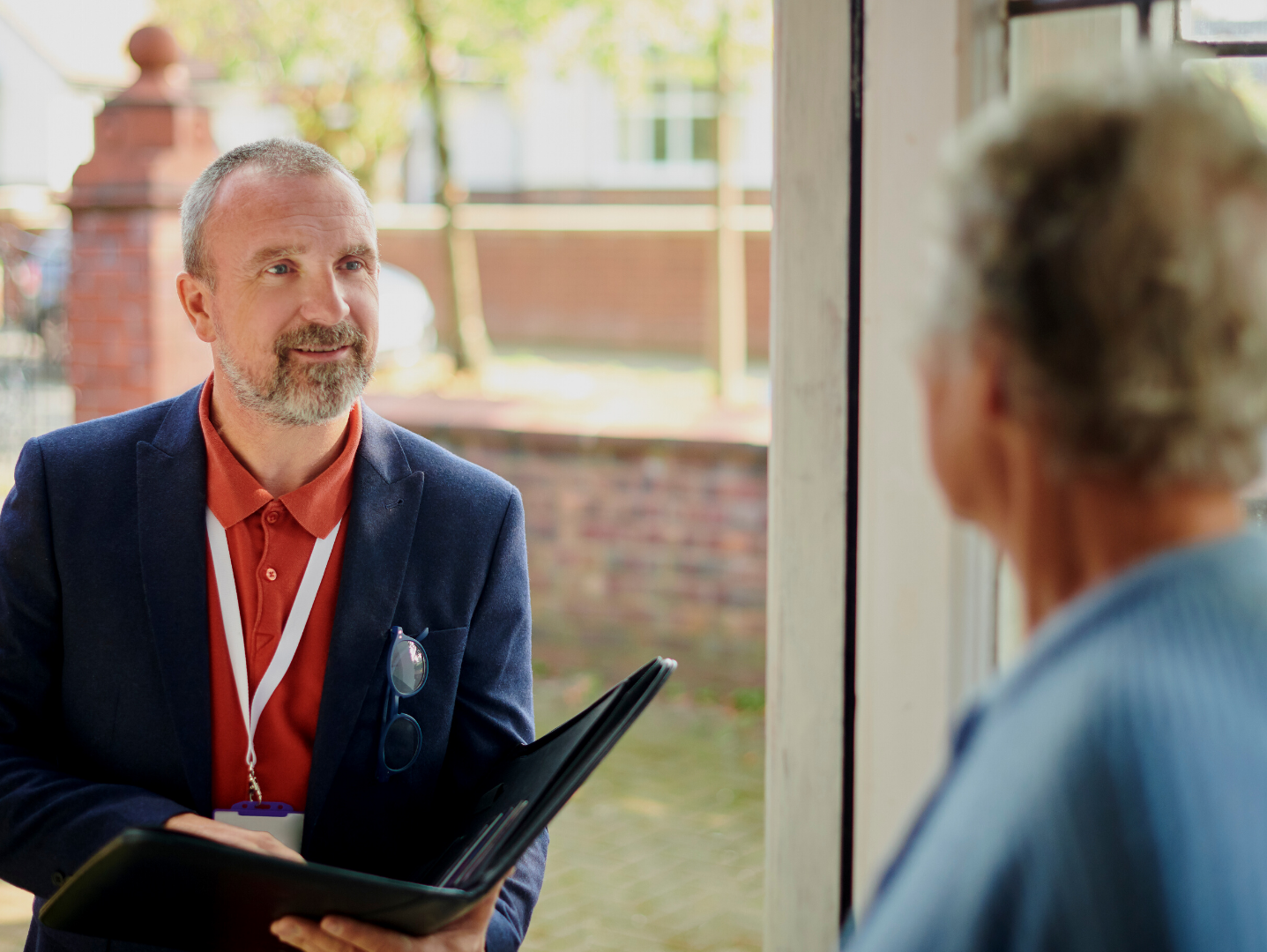 A man in a suit is holding a clipboard and talking to an older man.