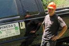 Worker in orange hard hat leaning on a black truck with a business sign on the door.